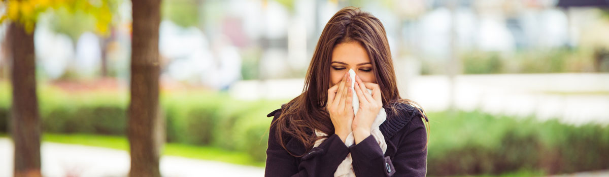 woman suffering from allergies blows her nose at a park Colorado Allergy & Asthma Centers
